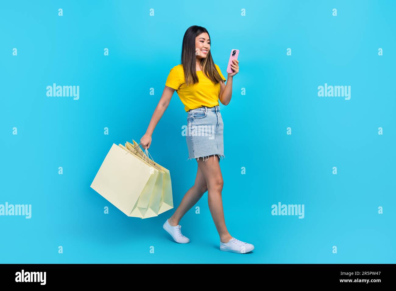 Pleine longueur jambes photo de belle jeune femme coréenne boutique en ligne asos marque téléphone marche avec des bonnes affaires isolées sur fond bleu de couleur Banque D'Images