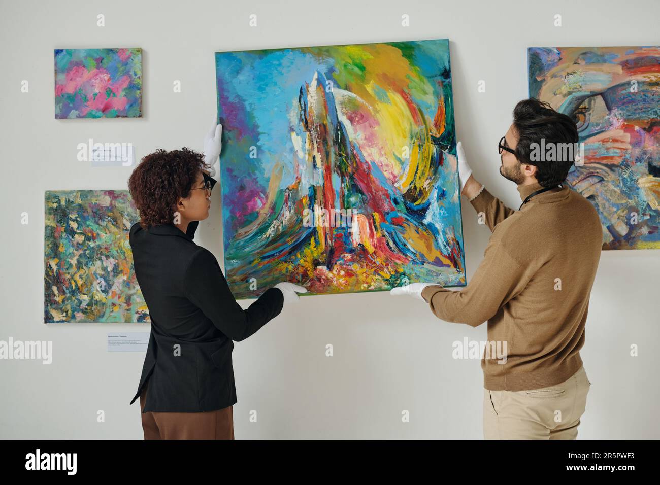 Deux employés qui pendent des peintures sur le mur, se préparent à une exposition d'art dans la galerie Banque D'Images