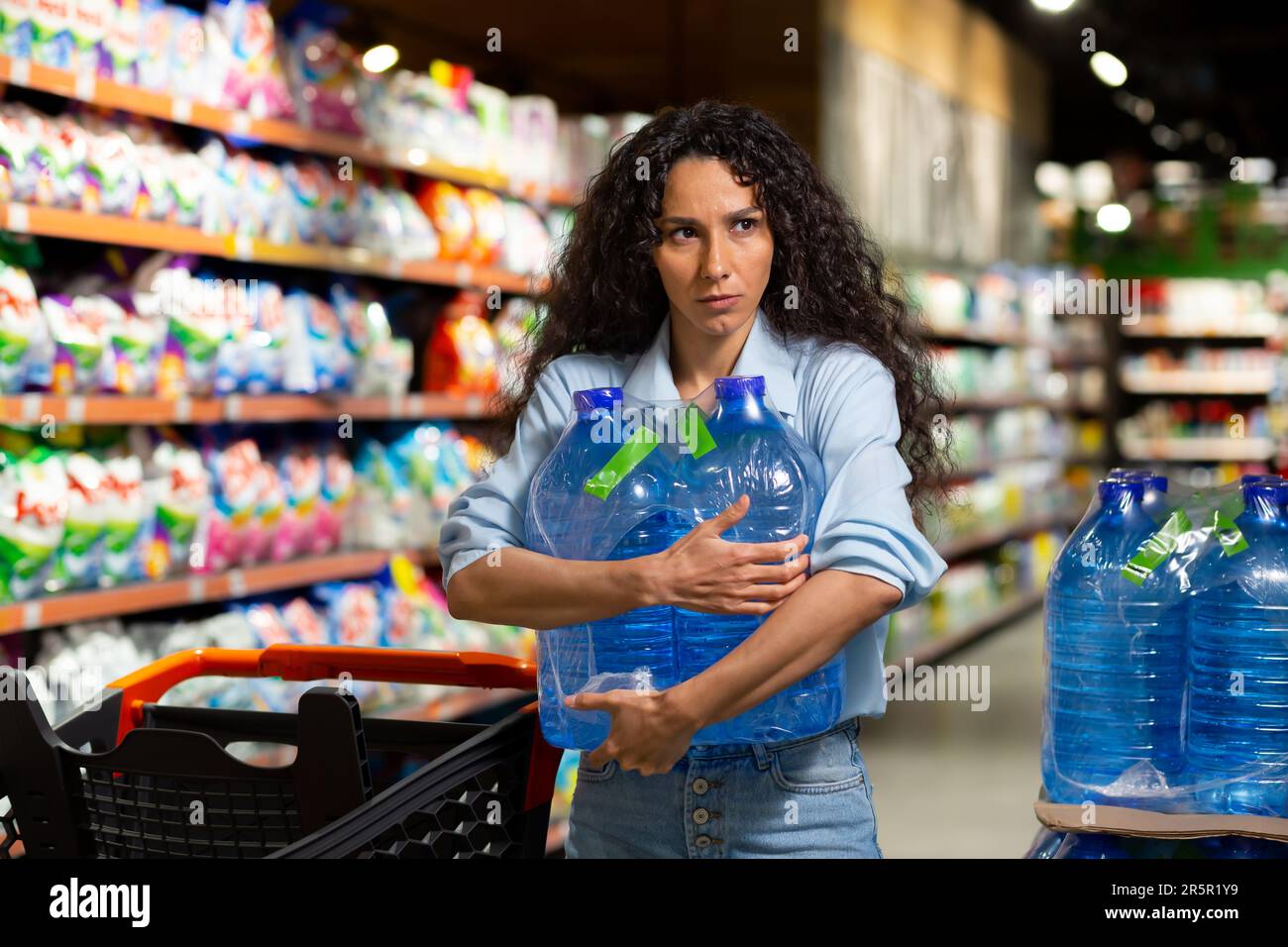 Une jeune femme achète des palettes d'eau dans un supermarché. Il le prend entre ses mains, le met dans un chariot. Panique pendant une pandémie, quarantaine Banque D'Images