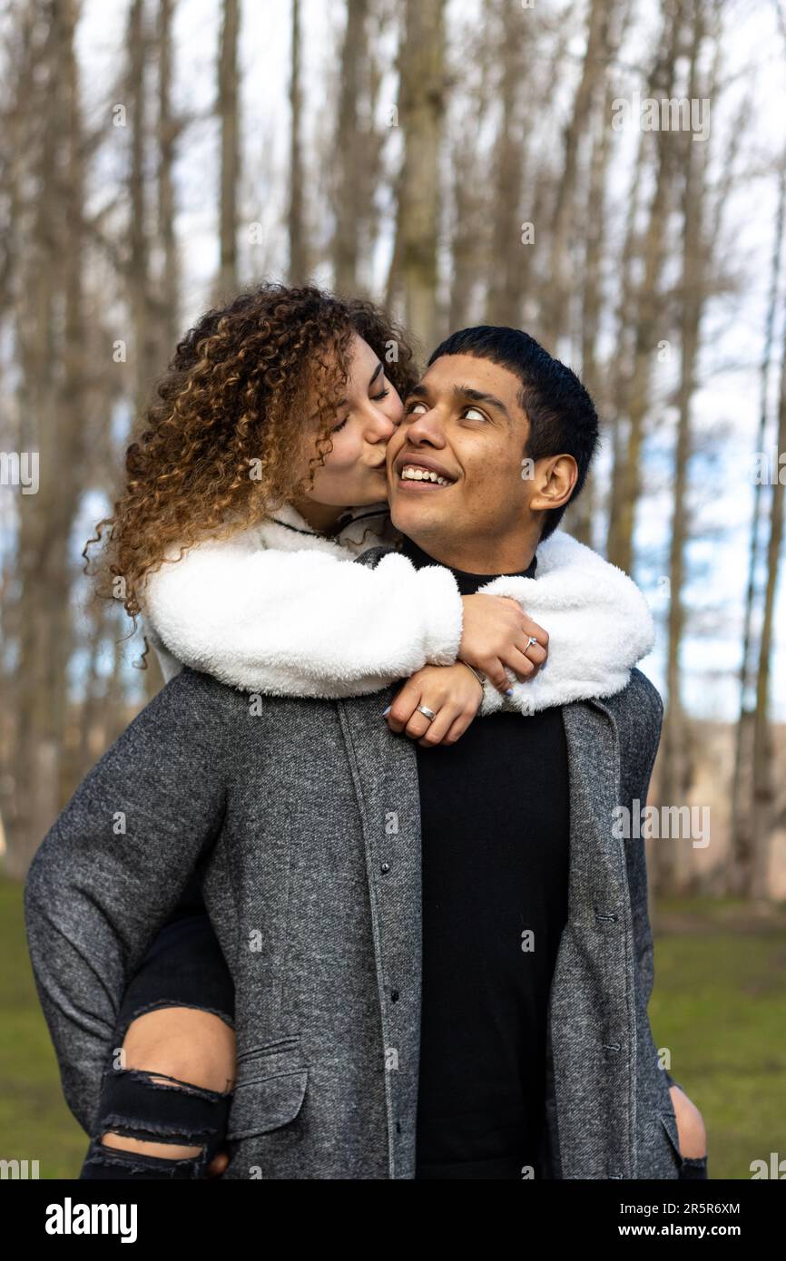 Un homme caucasien portant un t-shirt bleu, un Jean et des baskets blanches, embrasse une femme caucasienne portant une jupe et un haut blancs, comme ils se tiennent dans Banque D'Images