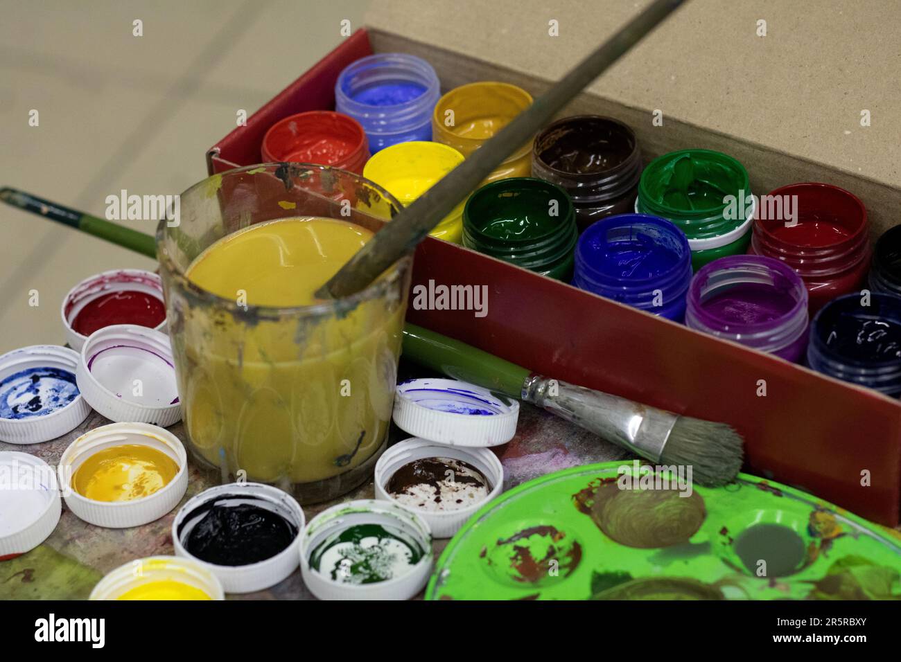 photo ouverte avec différentes couleurs de peintures et pinceaux et un verre d'eau sale Banque D'Images