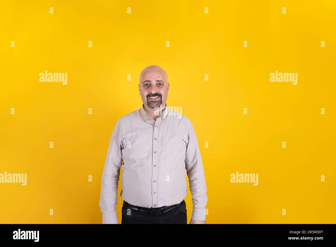 Portrait caucasien d'âge moyen d'un homme souriant. Plan de face de la figure paternelle masculine debout sur fond jaune isolé, espace de copie. Un mec barbu chauve Banque D'Images