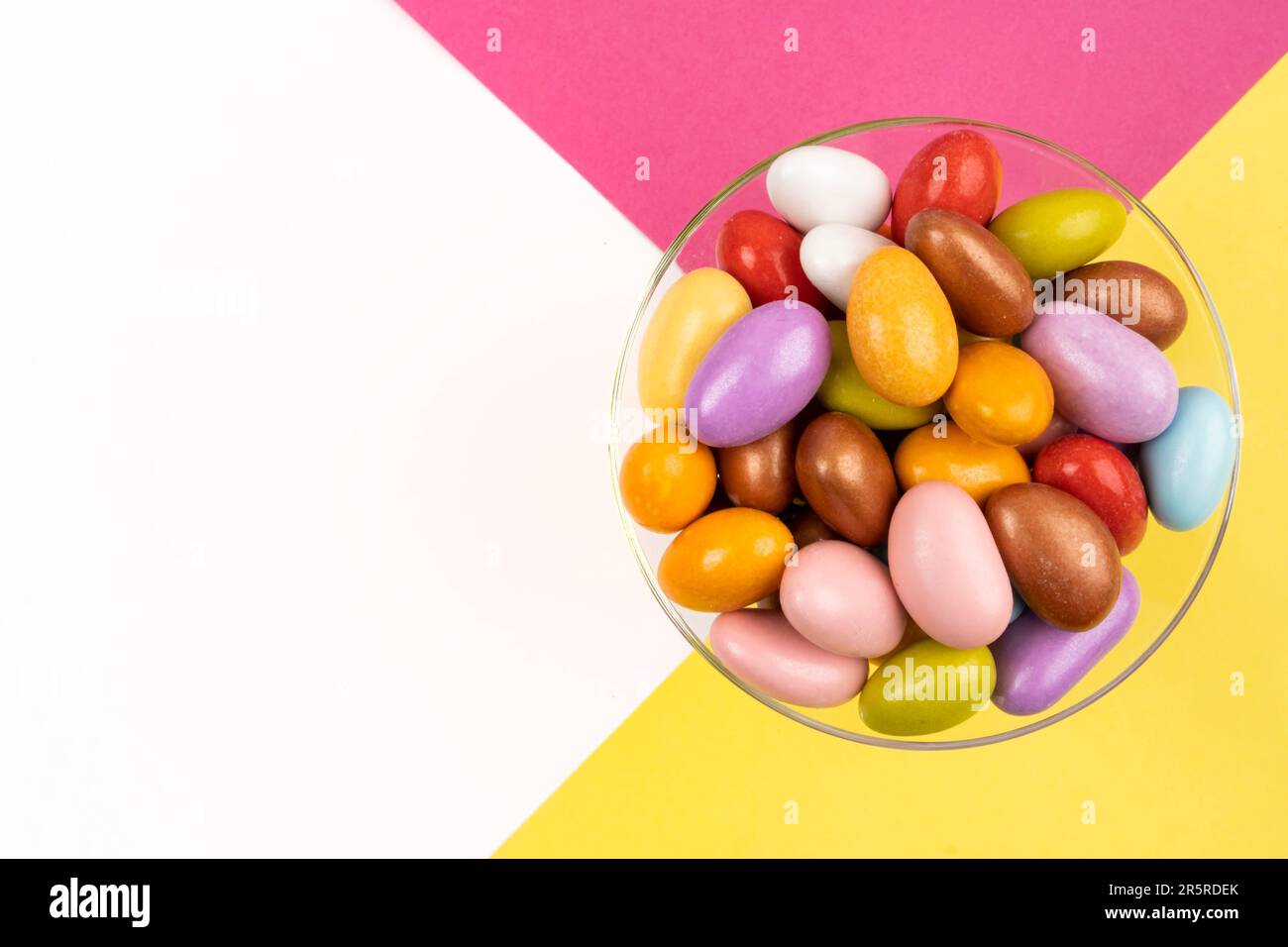 Image vue de dessus de bonbons aux amandes colorés. Bol en verre élégant. Espace copie blanc. Fond rose et jaune. Le concept de fête du sucre en turc. Banque D'Images