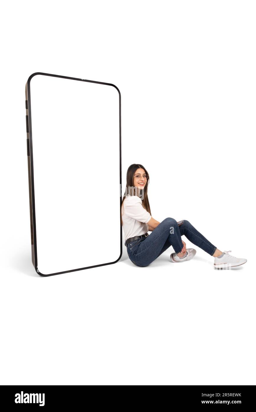 Concept de publicité d'application, brune jeune femme assise sur le sol, penchant grand smartphone énorme avec maquette d'écran vide. Banque D'Images