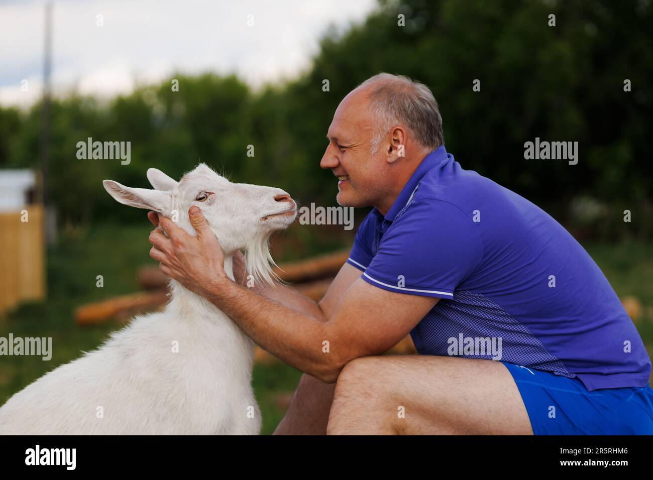 un homme d'âge moyen parle face à face à une chèvre blanche et sourit Banque D'Images