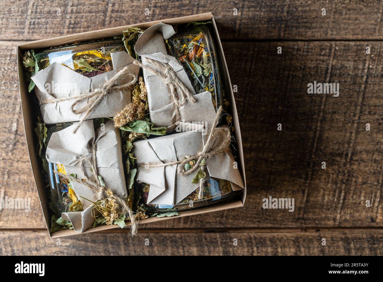 Quatre bocaux en verre avec fleurs sèches et tisane dans une boîte cadeau sur fond de bois, espace de copie, vue de dessus. Tisane Banque D'Images