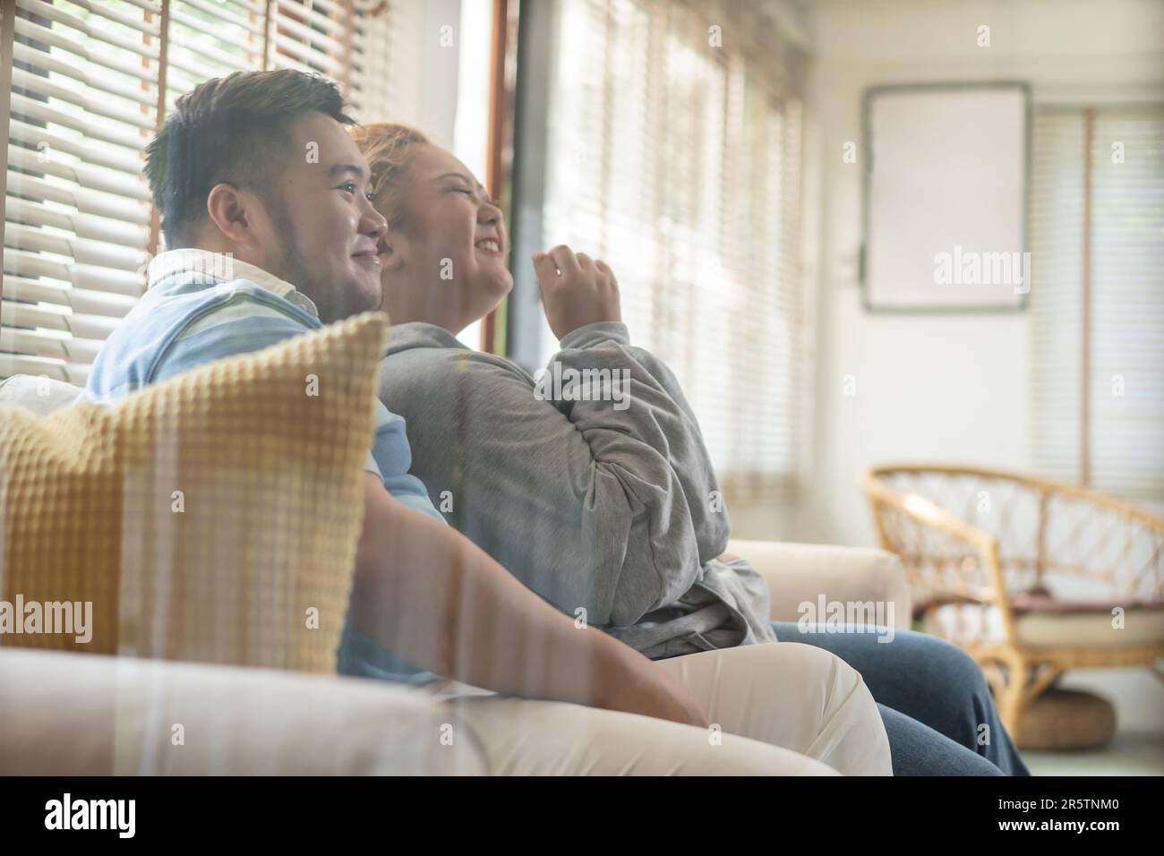 Un jeune couple asiatique de chubby regarde une série télévisée et un film sur le canapé dans le salon. Homme et femme qui s'amusent ensemble à la maison. Les gens rient et sourient ensemble Banque D'Images