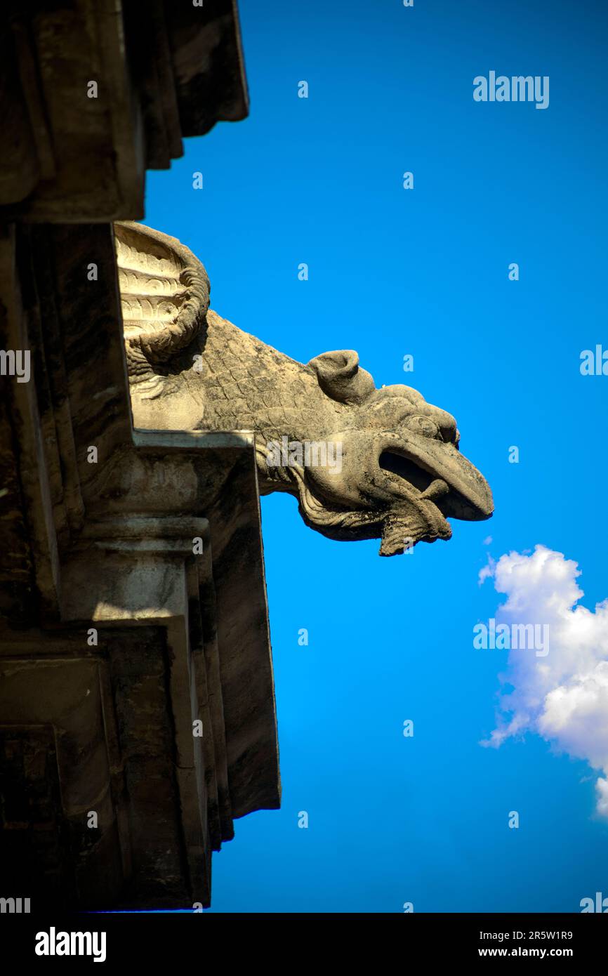 Gargouille de pierre en forme de créature aux dents pointues et aux ailes sur le corniche de la cathédrale de Santa Maria à Murcia, Espagne avec un nuage en t. Banque D'Images