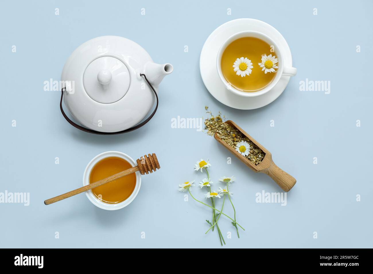 Théière et tasse de thé chaud à la camomille avec miel sur fond bleu pâle Banque D'Images