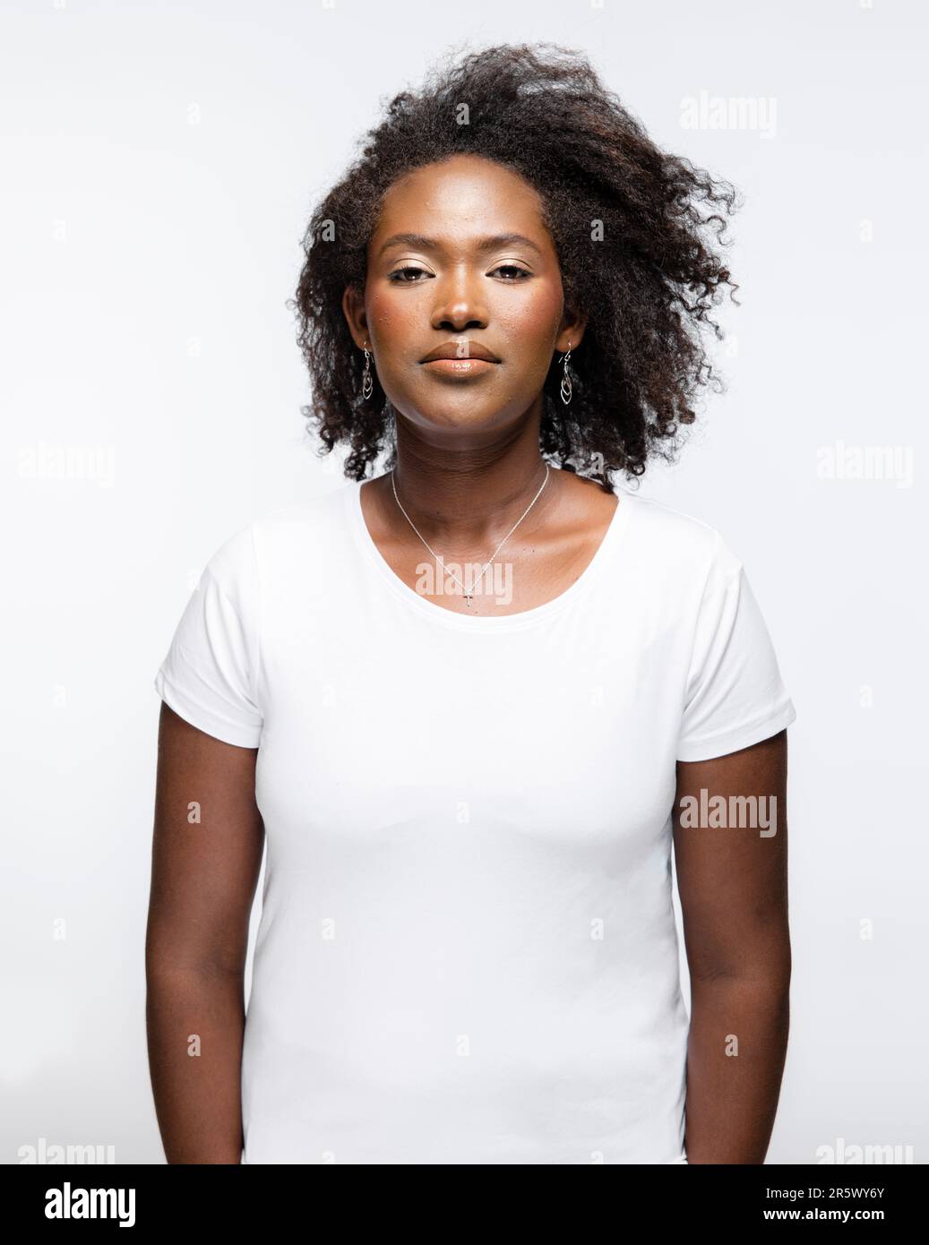 Une jeune femme adulte portant un t-shirt blanc debout avec confiance les mains sur les hanches, regardant directement l'appareil photo dans une personne déterminée et asser Banque D'Images