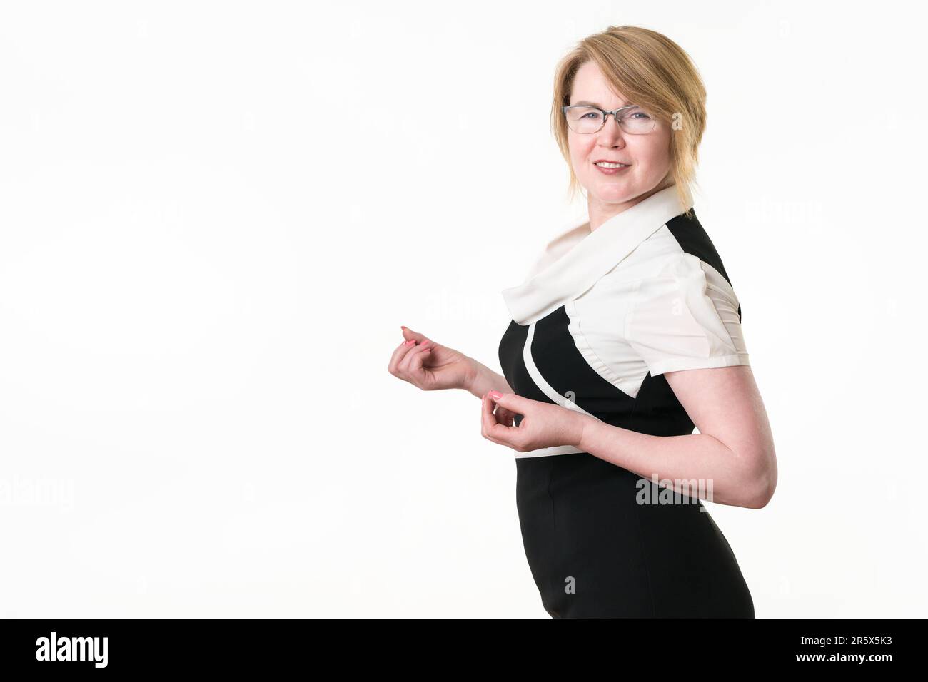 Portrait de femme blonde en lunettes vêtues de robe noire et blanche regardant l'appareil photo. Belle femme de 49 ans sincère souriant, posant sur blanc Banque D'Images