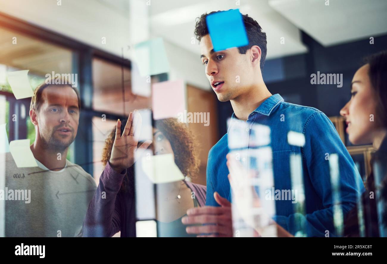 À venir avec la prochaine grande idée d'entreprise. un groupe de jeunes designers remue-méninges avec des notes sur un mur de verre dans un bureau. Banque D'Images