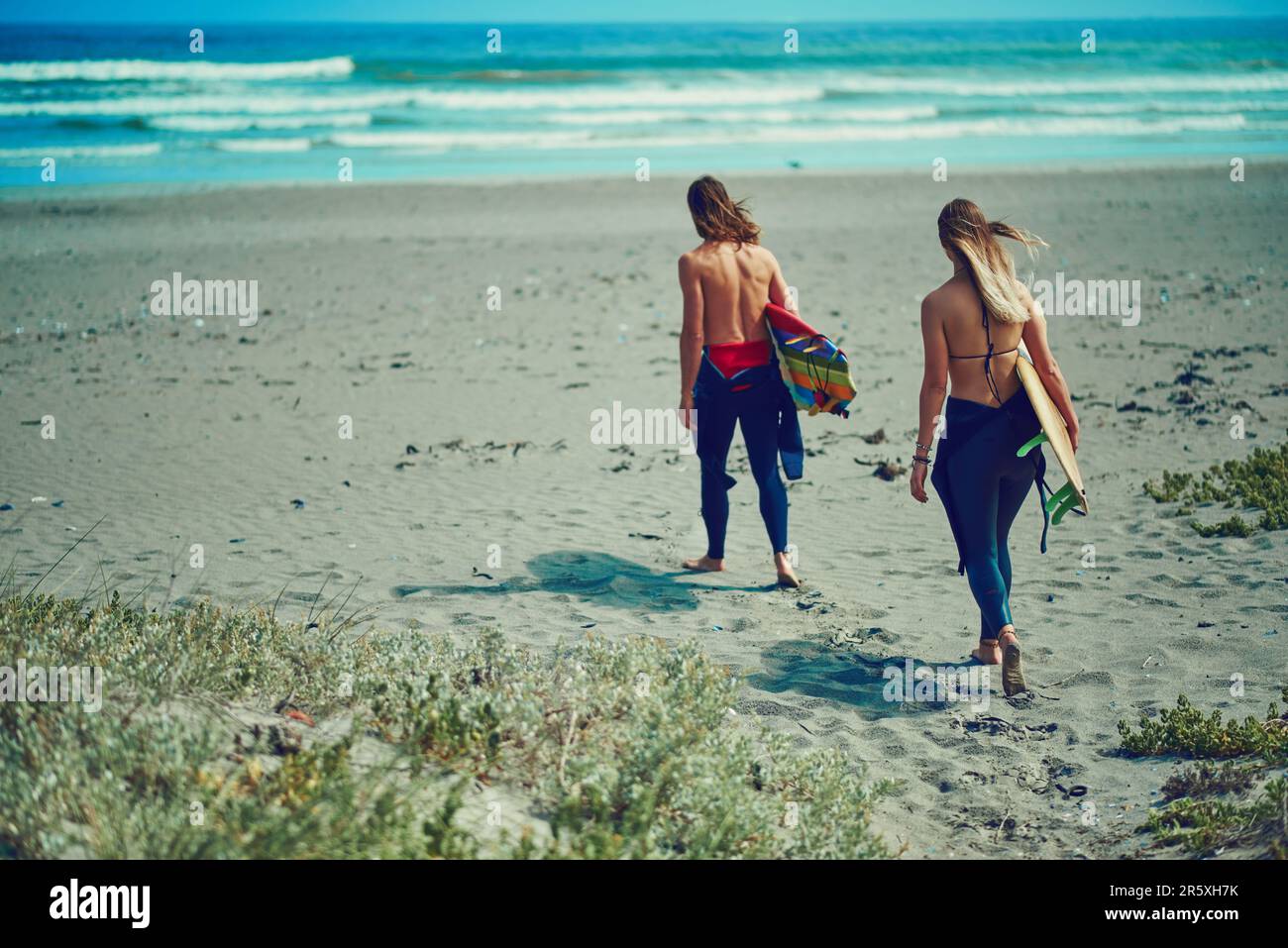 C'est là que le temps est resté immobile. un jeune couple qui marche sur la plage avec leurs planches de surf. Banque D'Images