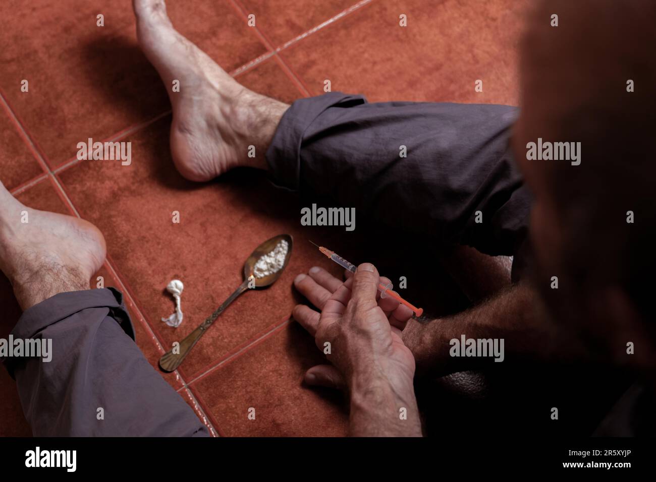 Vue de dessus d'un homme assis pieds nus sur le sol avec une seringue d'héroïne dans sa main concept de toxicomanie Banque D'Images