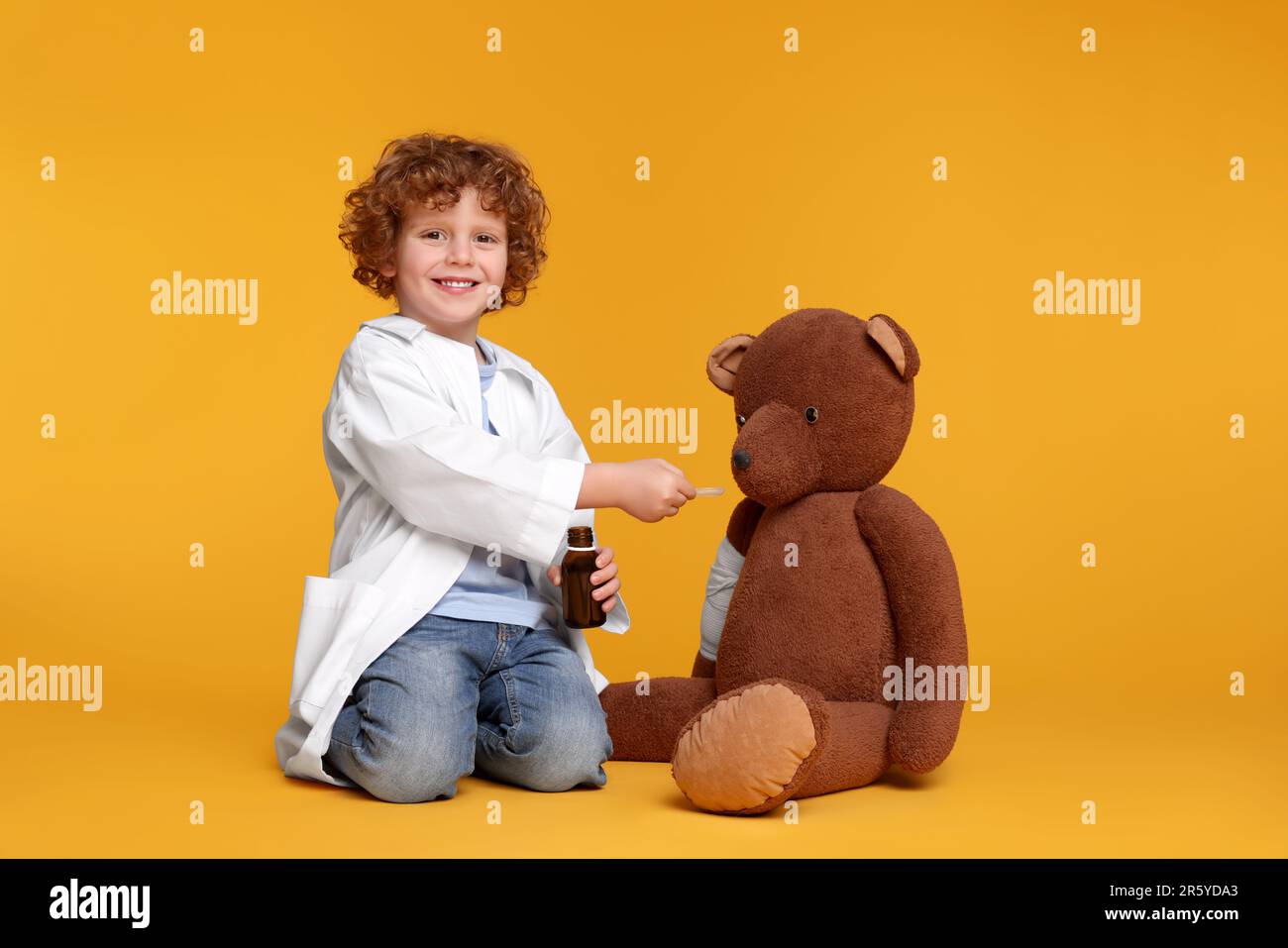 Petit garçon jouant docteur avec ours jouet sur fond jaune Banque D'Images
