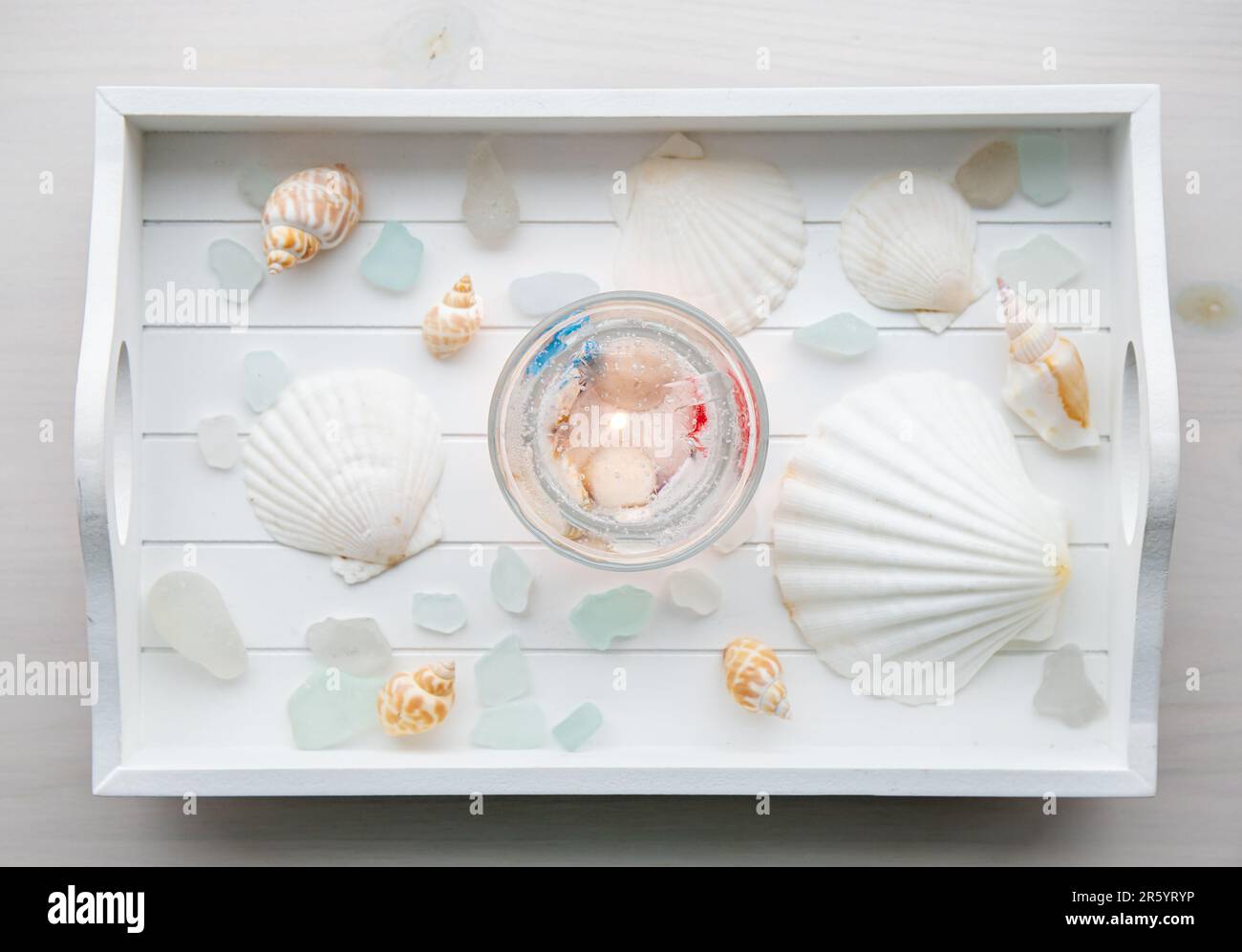 Au-dessus de la vue de la maison sous-marin seashell gel transparent cire bougie à l'intérieur transparent tasse. Belle bougie sur plateau en bois blanc avec verre de mer et coquillages. Banque D'Images