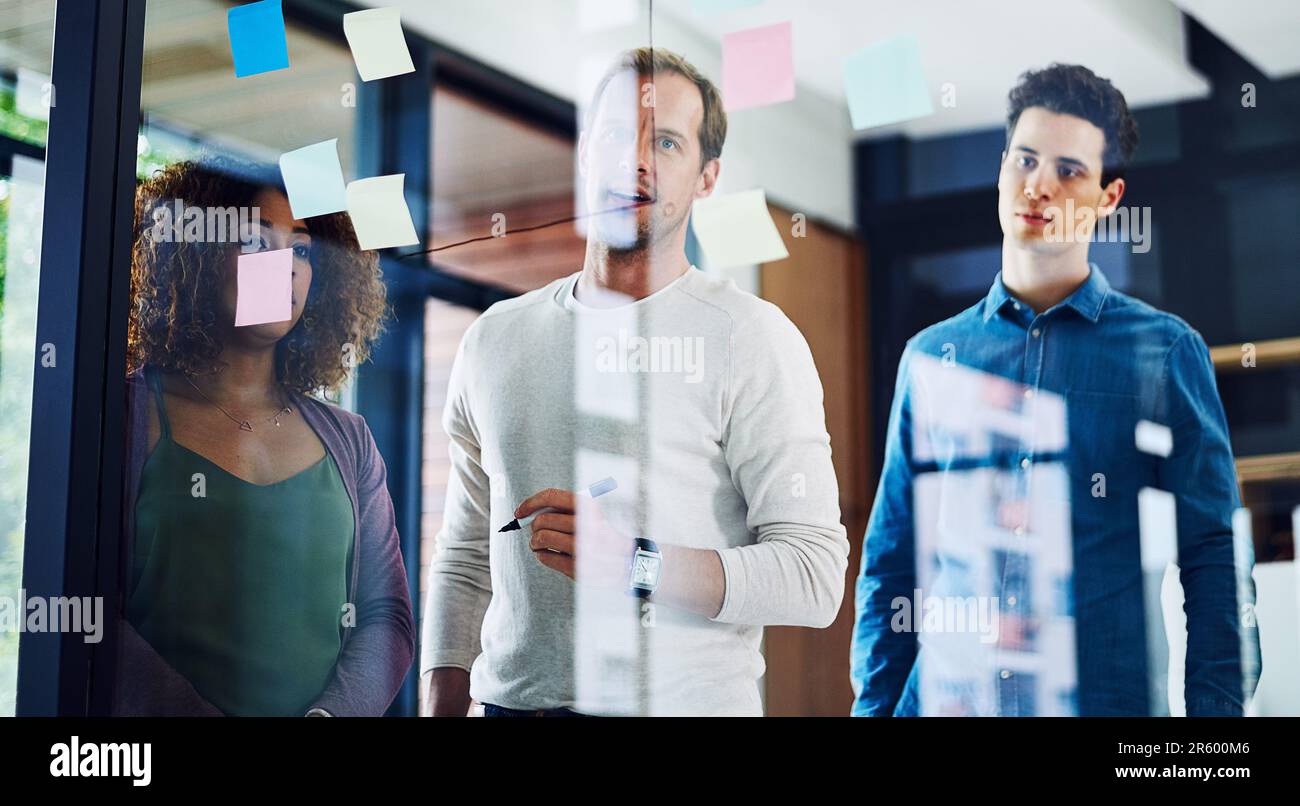 HES a eu de grands projets à présenter. un groupe de jeunes designers remue-méninges avec des notes sur un mur de verre dans un bureau. Banque D'Images