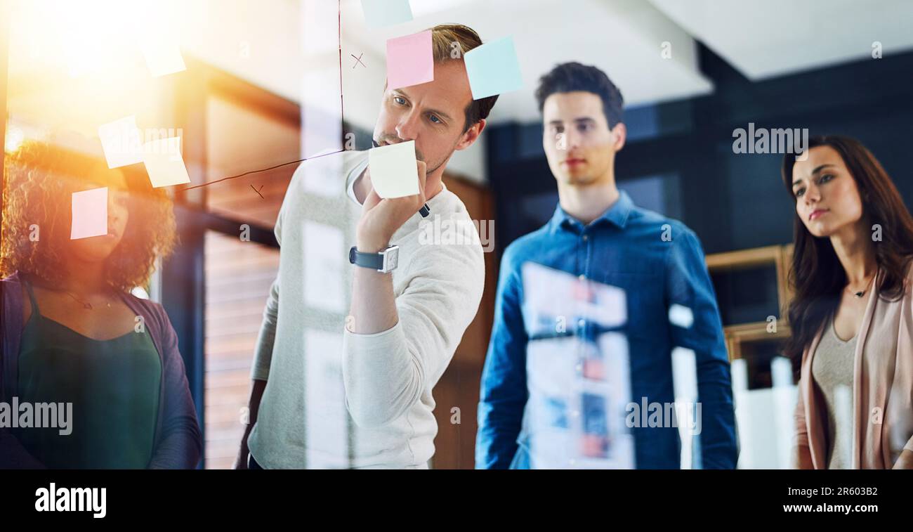 Réaliser ensemble leurs grandes idées audacieuses. un groupe de jeunes designers remue-méninges avec des notes sur un mur de verre dans un bureau. Banque D'Images