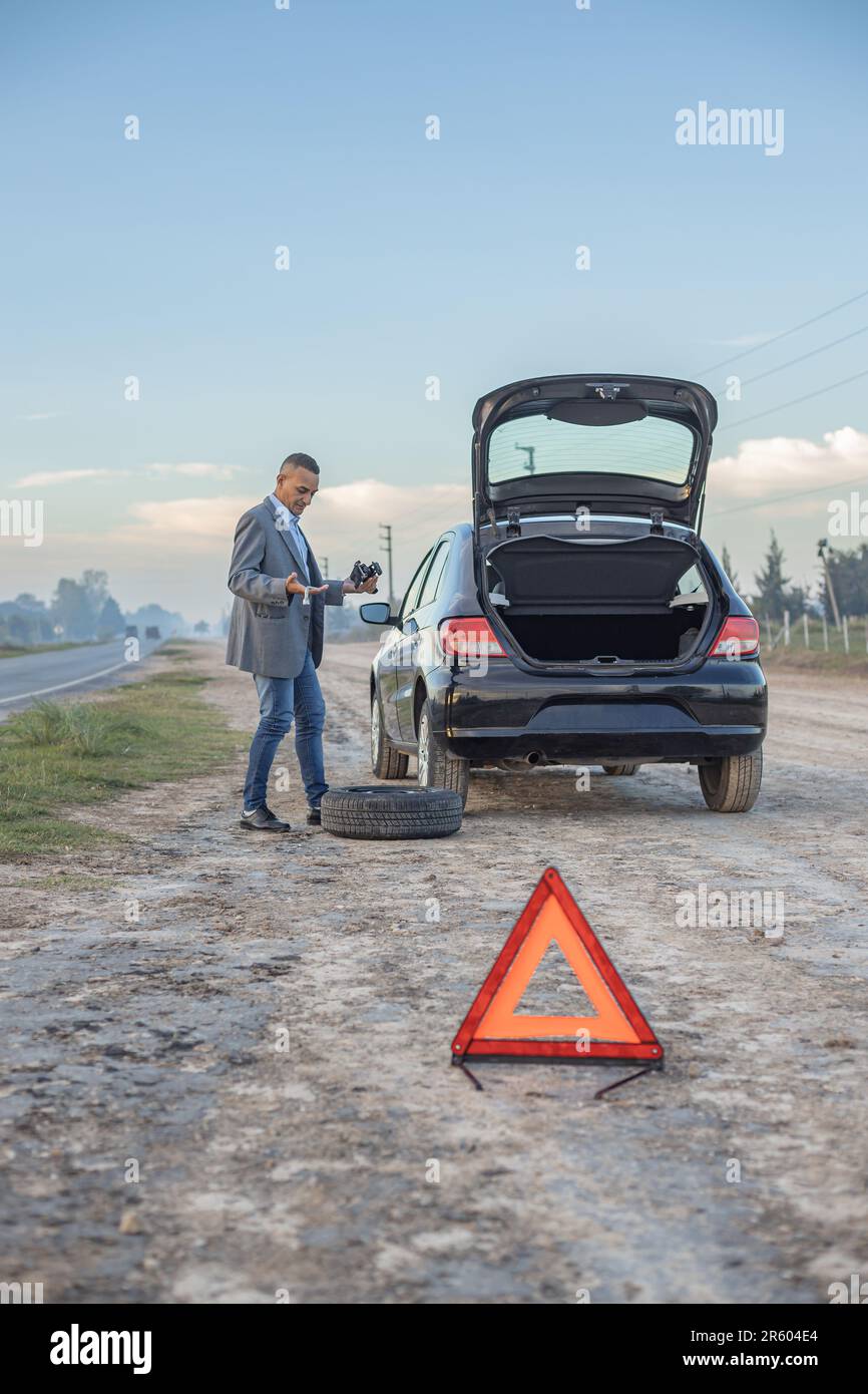 Confus latino homme essaie de changer le pneu à plat de sa voiture. Banque D'Images