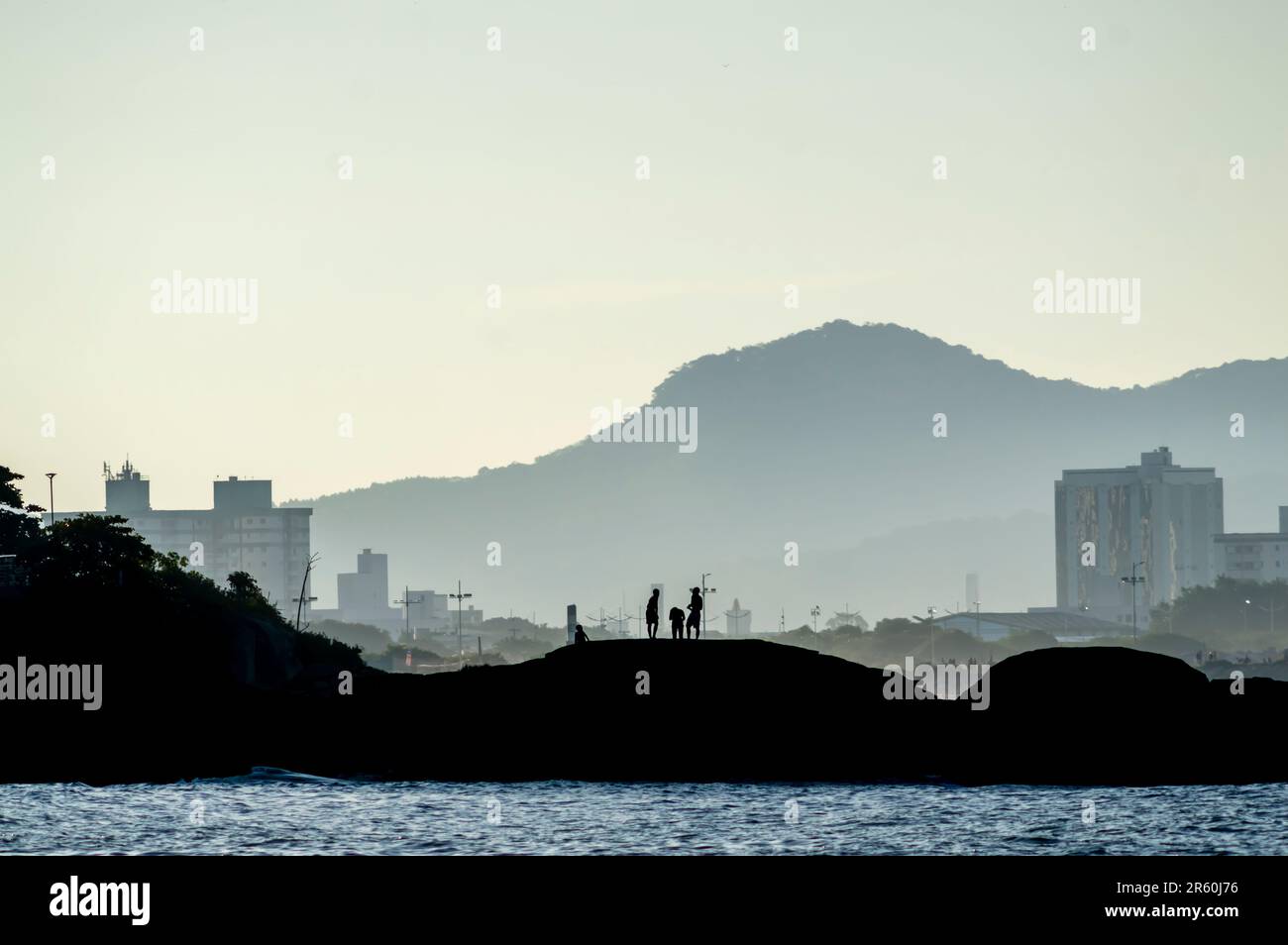 Enfants jouant sur une île au bord de la mer, en fin d'après-midi avec les montagnes en arrière-plan et l'océan devant, concept de plaisir sur la plage, seulement le silho Banque D'Images