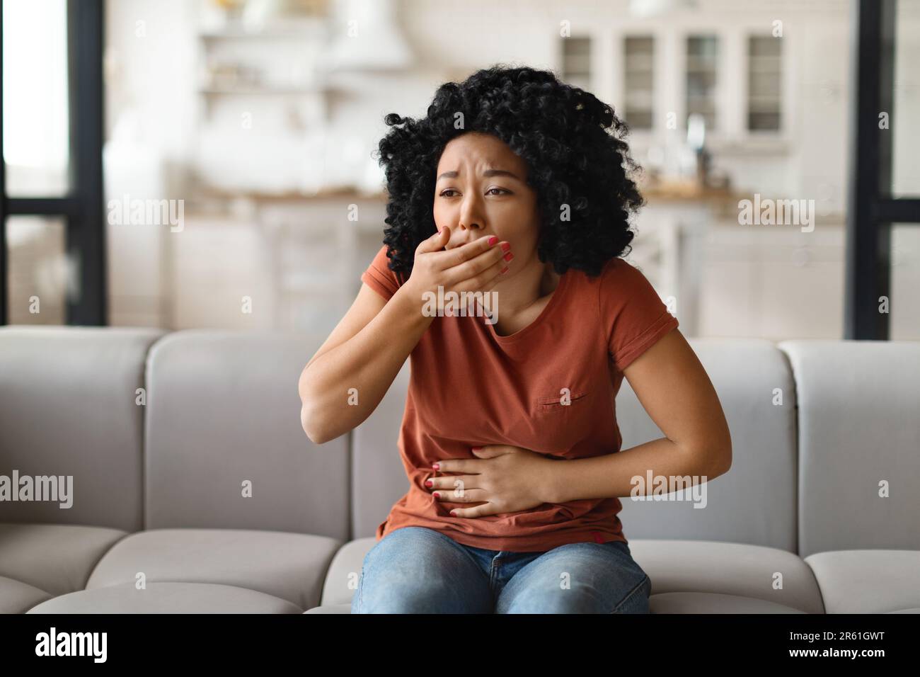 Jeune femme noire souffrant de nausées lorsqu'elle est assise sur un canapé à la maison Banque D'Images