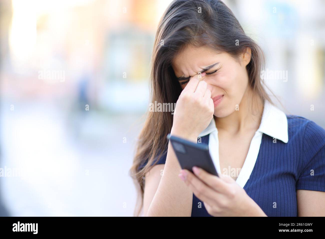 Femme stressée souffrant d'eyestrein tenant le téléphone dans la rue Banque D'Images