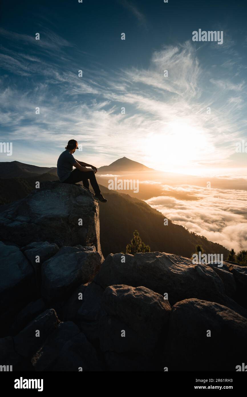 Jeune homme assis sur le rocher d'une montagne observant le magnifique paysage de Teide pic au coucher du soleil pendant son voyage d'aventure sur l'île des Canaries o Banque D'Images