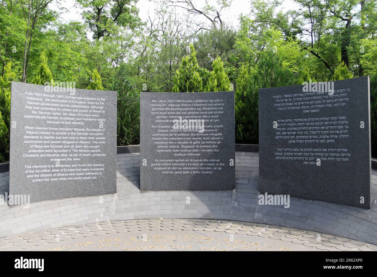 Le Mémorial de l'Holocauste à Tirana, en Albanie, rend hommage à plus de 6 millions de vies perdues et commémore le courage des citoyens albanais qui ont bravement travaillé pour sauver les Juifs des forces nazies. Le mémorial est bien placé à l'entrée artificielle du lac du Grand Parc de Tirana. Trois grands panneaux de granit incurvés placés dans une berme pavée légèrement inclinée créent un lieu de soudure pour le souvenir et la réflexion. Le lettrage en métal incrusté le long des pavés de granit cite le Talmud: “Whoever sauve une vie, sauve le monde entier”. Banque D'Images