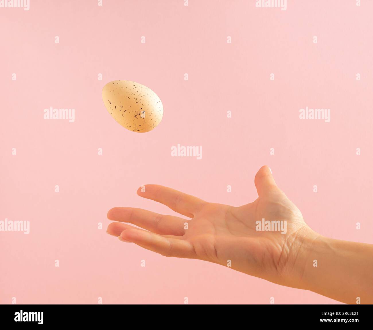 La main de la femme jette un œuf blanc sur fond rose pastel. Concept de Pâques minimal. Banque D'Images