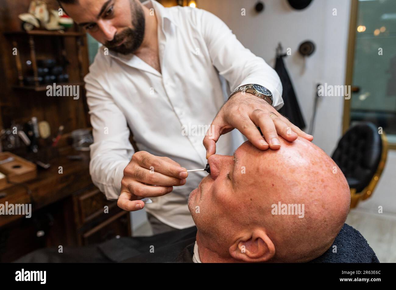 Un homme à tête blanche assis dans une chaise de coiffeur tandis qu'un coiffeur enlève les cheveux du nez Banque D'Images