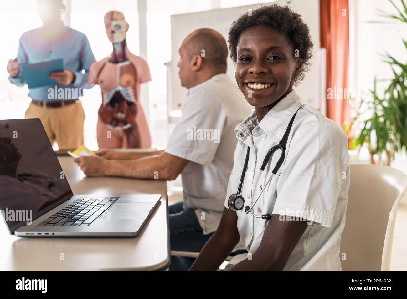 Une femme africaine dirige un atelier d'engagement dans la salle de réunion de la clinique. Elle sourit alors qu'elle interagit avec ses collègues, ordinateur portable à portée de main. Divers professionnels de la santé Banque D'Images