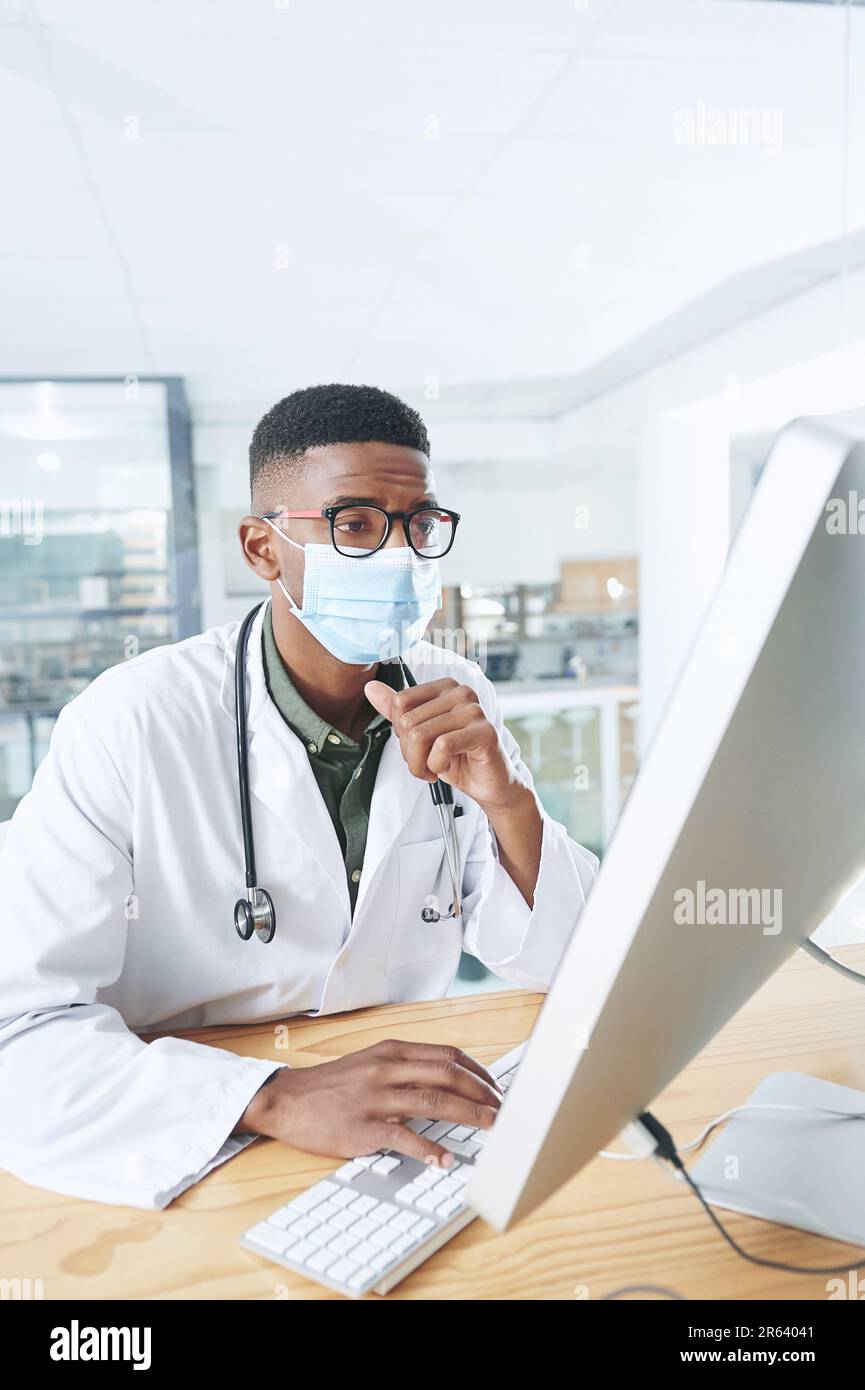 Je m'inquiète un peu de ces données. un jeune médecin portant un masque et assis dans son bureau à la clinique tout en utilisant un ordinateur. Banque D'Images