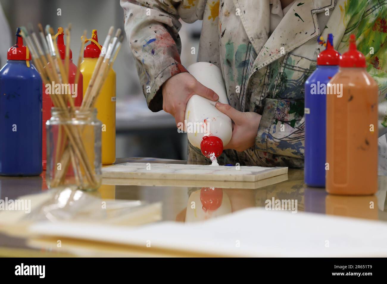 Un artiste ou un étudiant en art visuel dans le salon de l'art écurant ou versant de la peinture acrylique d'une bouteille blanche sur une palette de peinture. Salle de classe organisée. AR Banque D'Images