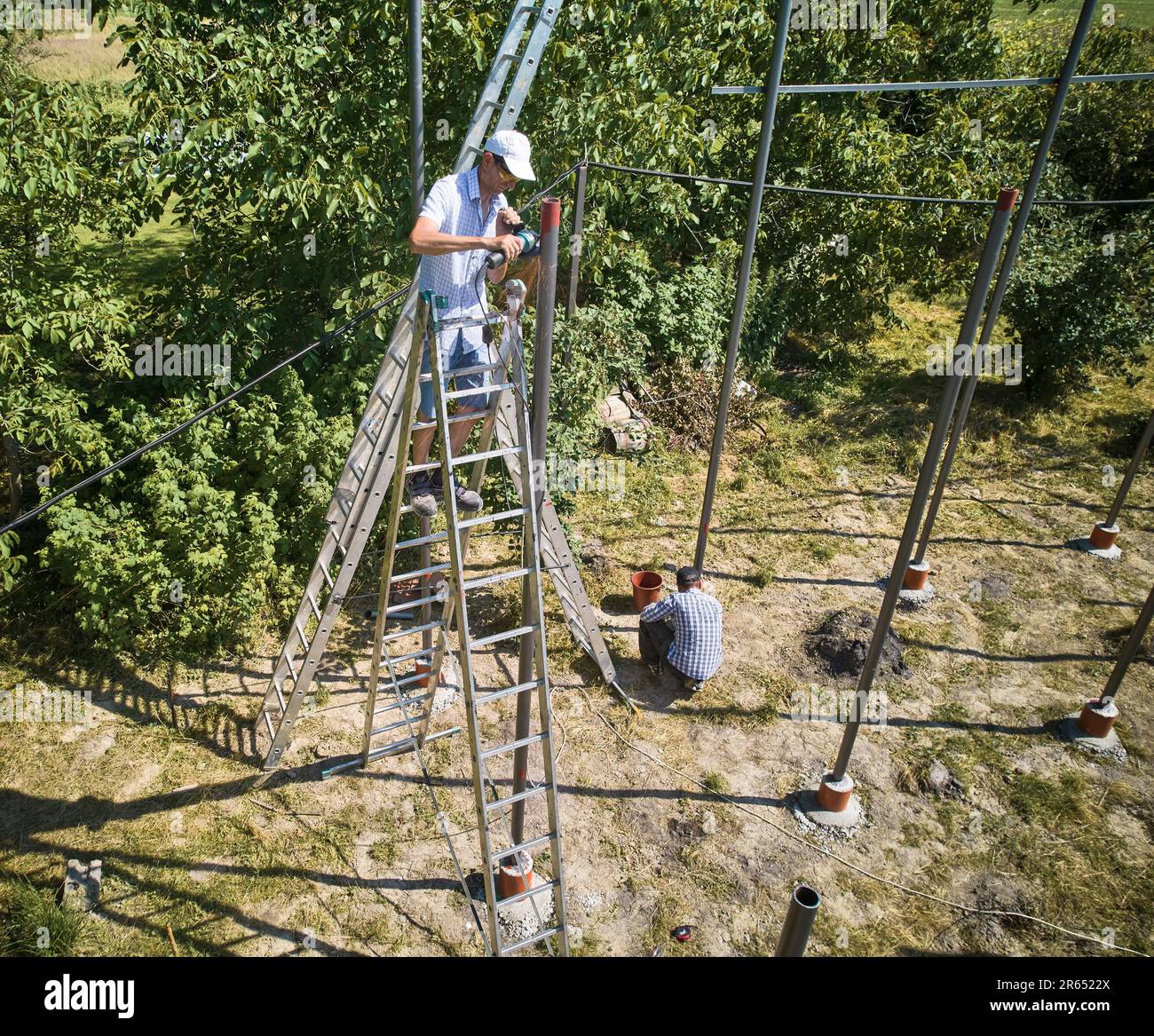 Travailleur debout sur un escalier et coupant une poutre métallique avec une meuleuse pour l'installation de panneaux solaires. Systèmes photovoltaïques montés au sol. Les modules solaires sont maintenus en place par des racks ou des cadres. Banque D'Images