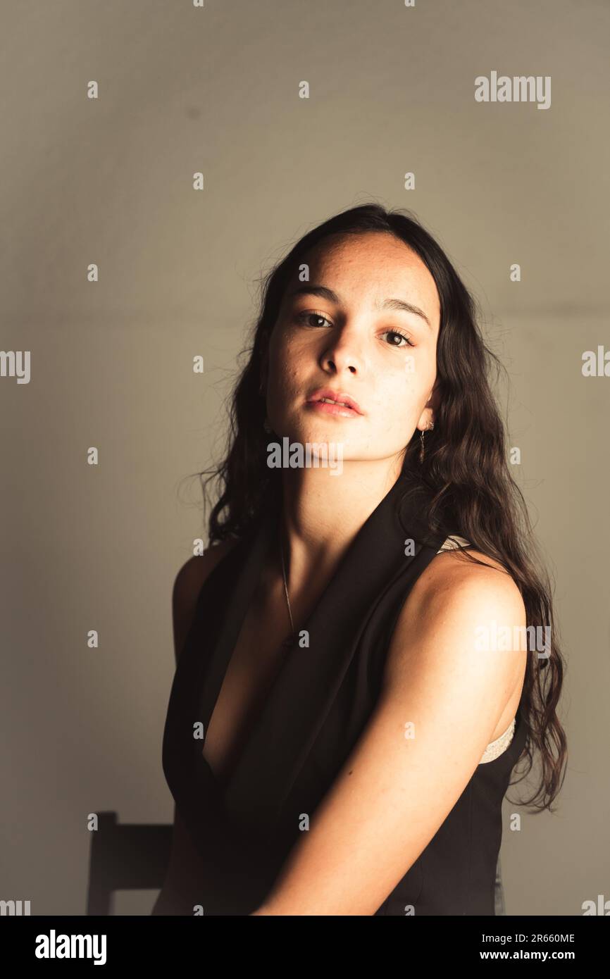 Une femme adulte, d'une beauté frappante, assise au-dessus d'une chaise devant un mur de fond Banque D'Images