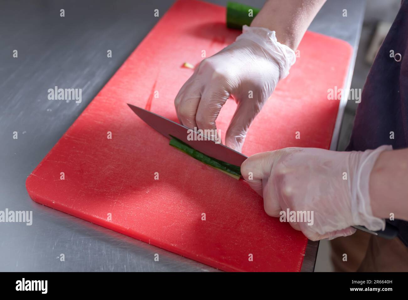 Le cuisinier coupe le concombre pour les petits pains à sushis sur un tableau rouge. Photo de haute qualité Banque D'Images