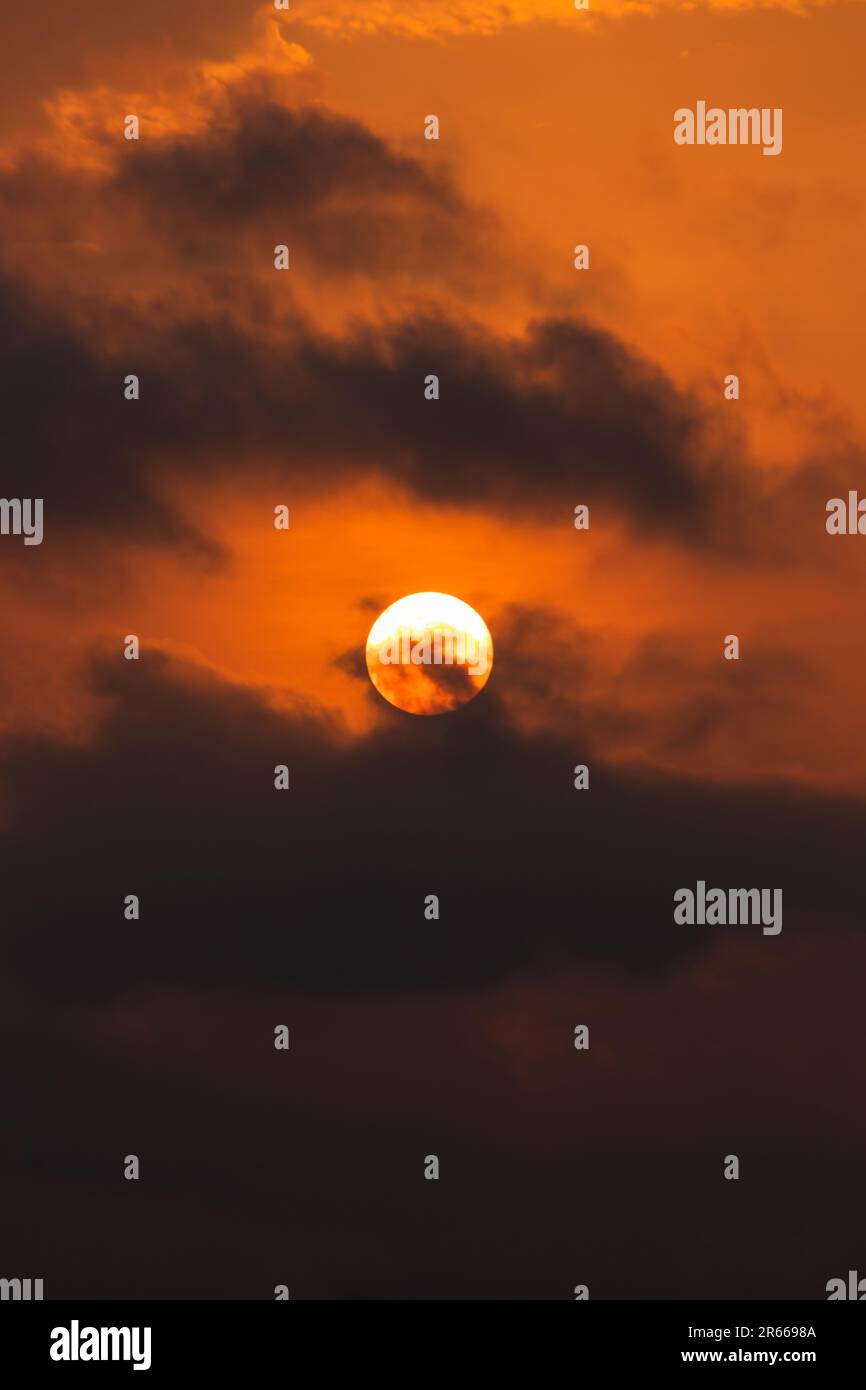 L'intense lueur orange du coucher de soleil projette une teinte spectaculaire sur les nuages et la lune dans cette scène nature grandiose. Banque D'Images