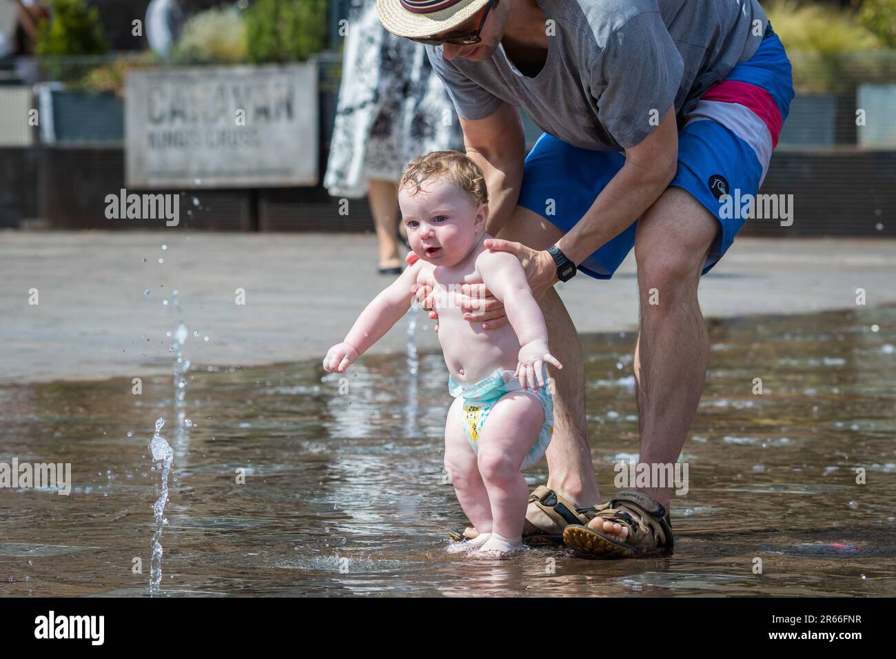 Londres, Royaume-Uni - 21 juin 2023 - vague de chaleur à Londres, père aidant son enfant à jouer avec de l'eau aux fontaines Granary Square à Kings Cross Banque D'Images