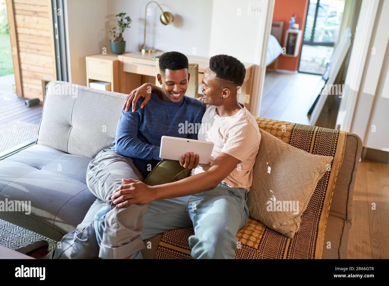 Un jeune garçon gay heureux qui se serre et utilise une tablette numérique sur le canapé Banque D'Images