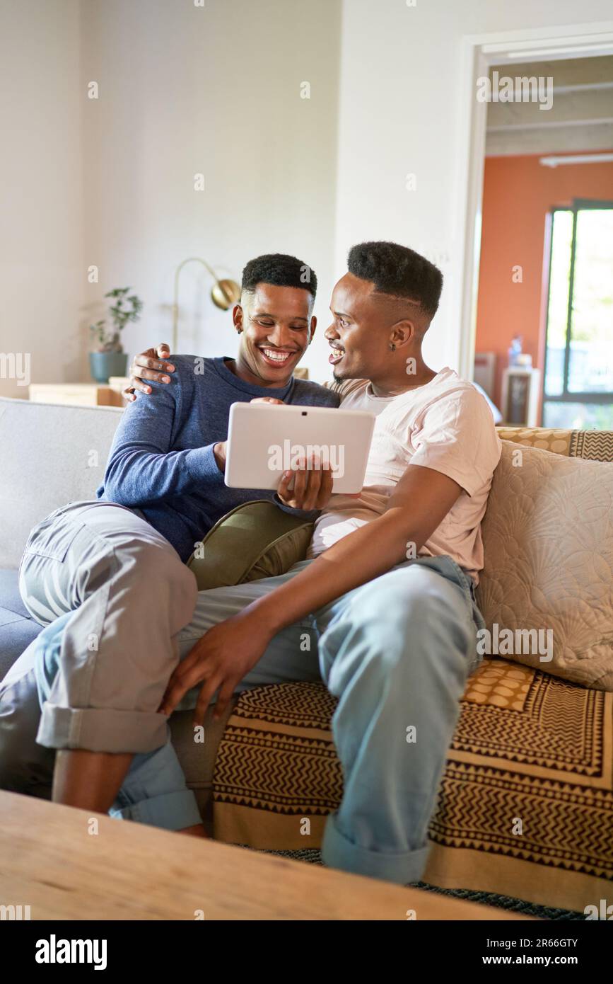Un jeune homme gay heureux en utilisant une tablette numérique sur le canapé du salon Banque D'Images