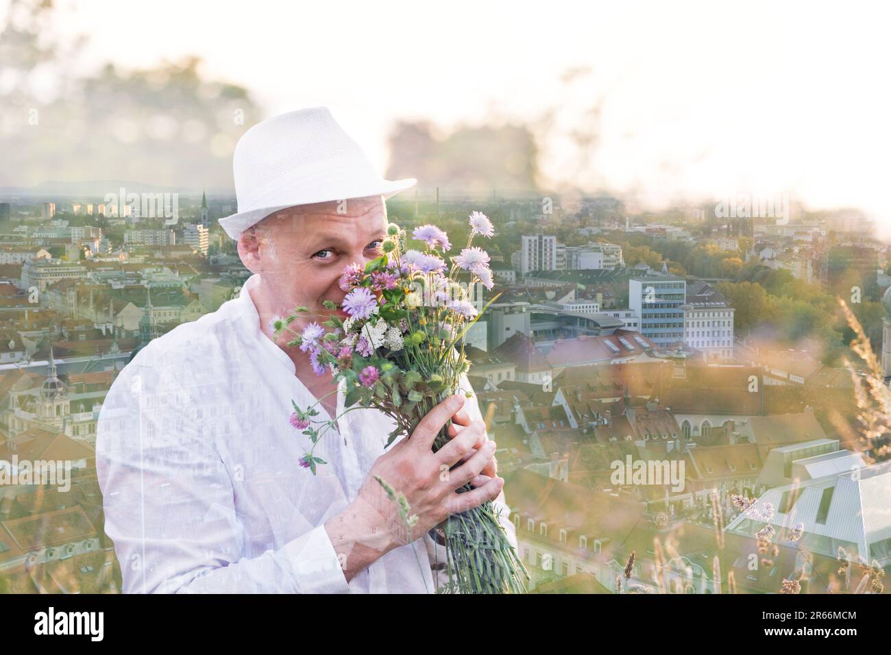 Double exposition. Un beau homme renifle des fleurs dans un bouquet et regarde la caméra. Sur la toile de fond d'une ville prise d'une hauteur. Foc différent Banque D'Images