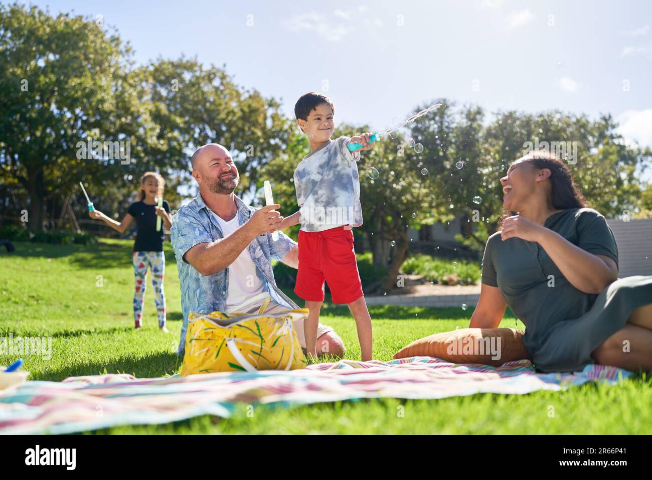 Bonne famille jouant avec des bulles dans le parc ensoleillé d'été Banque D'Images