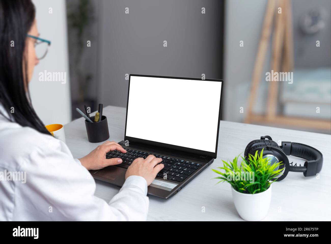Une jeune fille concentrée travaille sur un ordinateur portable avec un écran isolé pour la maquette. Ambiance professionnelle sur un bureau Banque D'Images