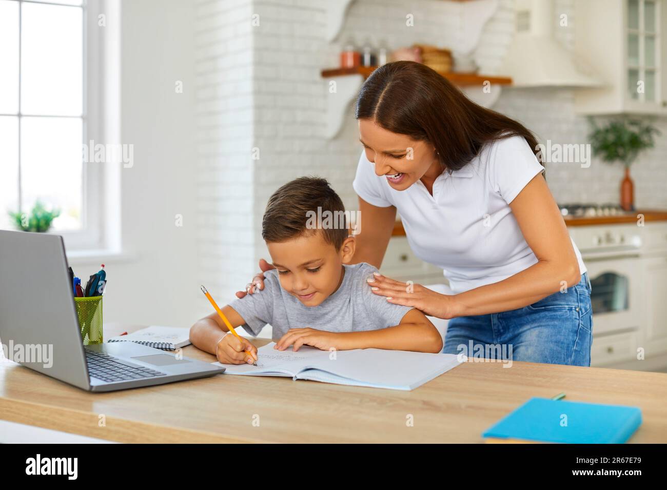 Une maman souriante aide son fils à faire ses devoirs pendant qu'il étudie en ligne à l'aide d'un ordinateur portable. Banque D'Images