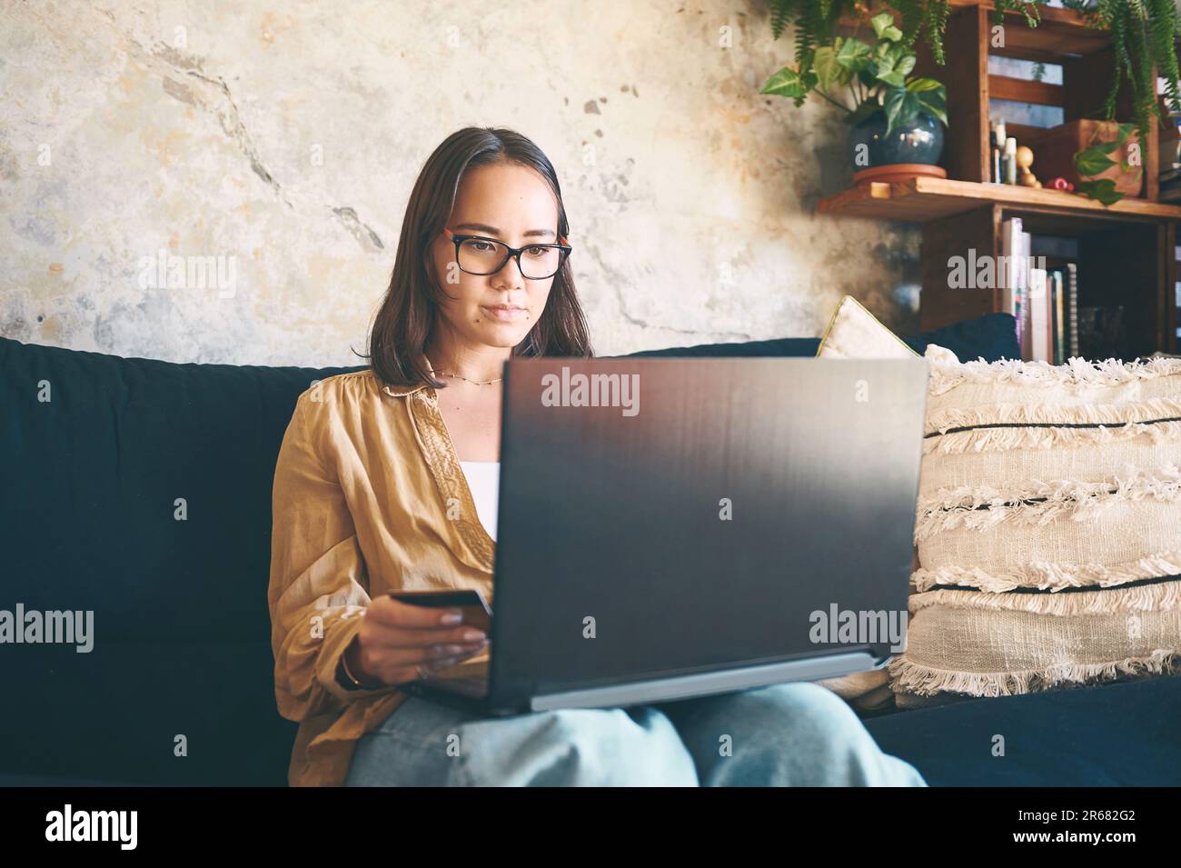 Lorsque le nouveau stock arrive, la coque doit être en avance sur la ligne. une jeune femme utilisant un ordinateur portable et une carte de crédit sur le canapé à la maison. Banque D'Images