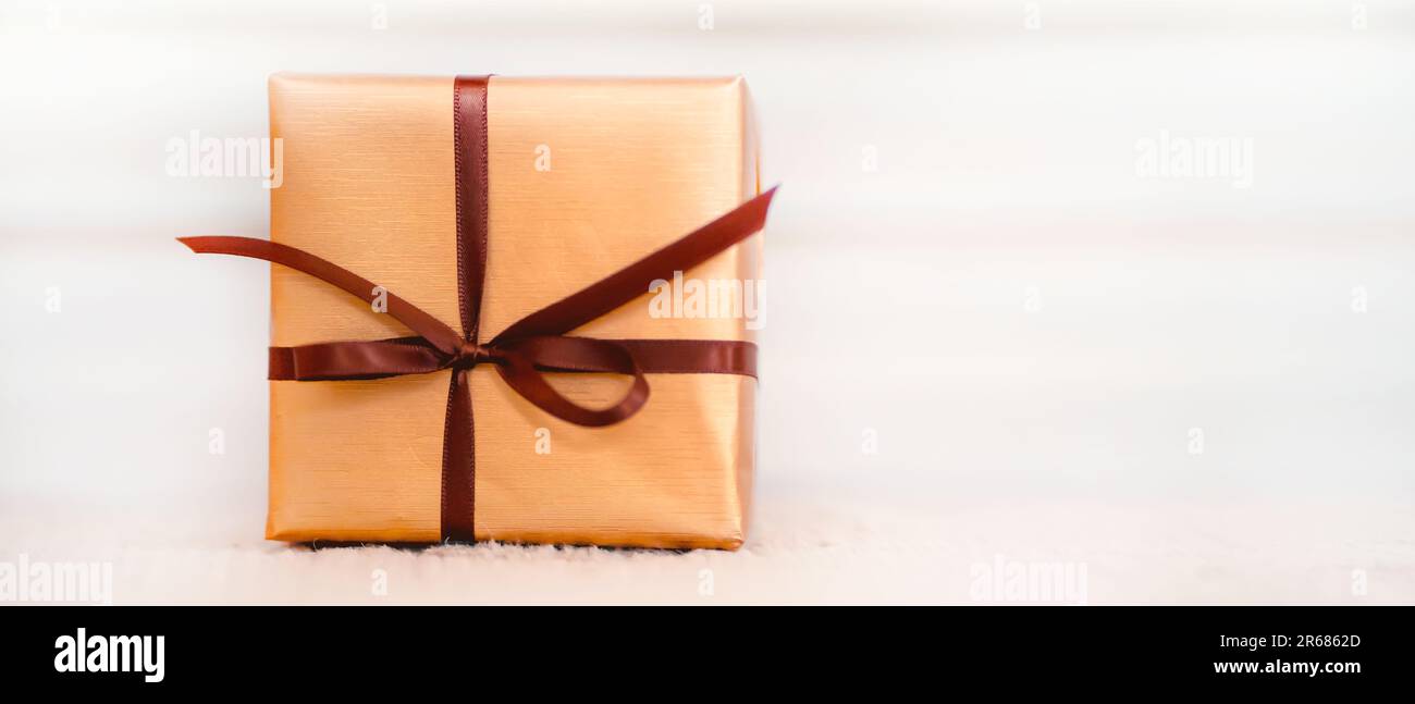 Un joli cadeau dans un élégant emballage doré, attaché avec un ruban fin,  vue rapprochée avec un espace pour les copies. Un concept créatif de  célébration et de préoccupation, t Photo Stock -