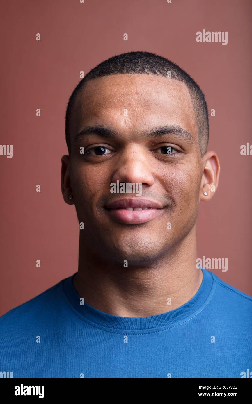 Portrait frontal d'un jeune afro-américain souriant, musclé, cheveux rasés, contour d'oreille en forme de losange, fond marron Banque D'Images