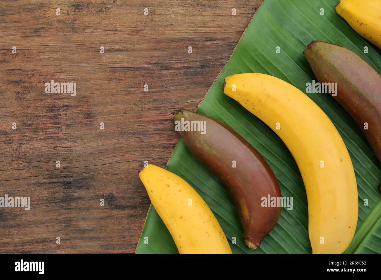 Différents types de bananes et feuilles fraîches sur table en bois, plat. Espace pour le texte Banque D'Images