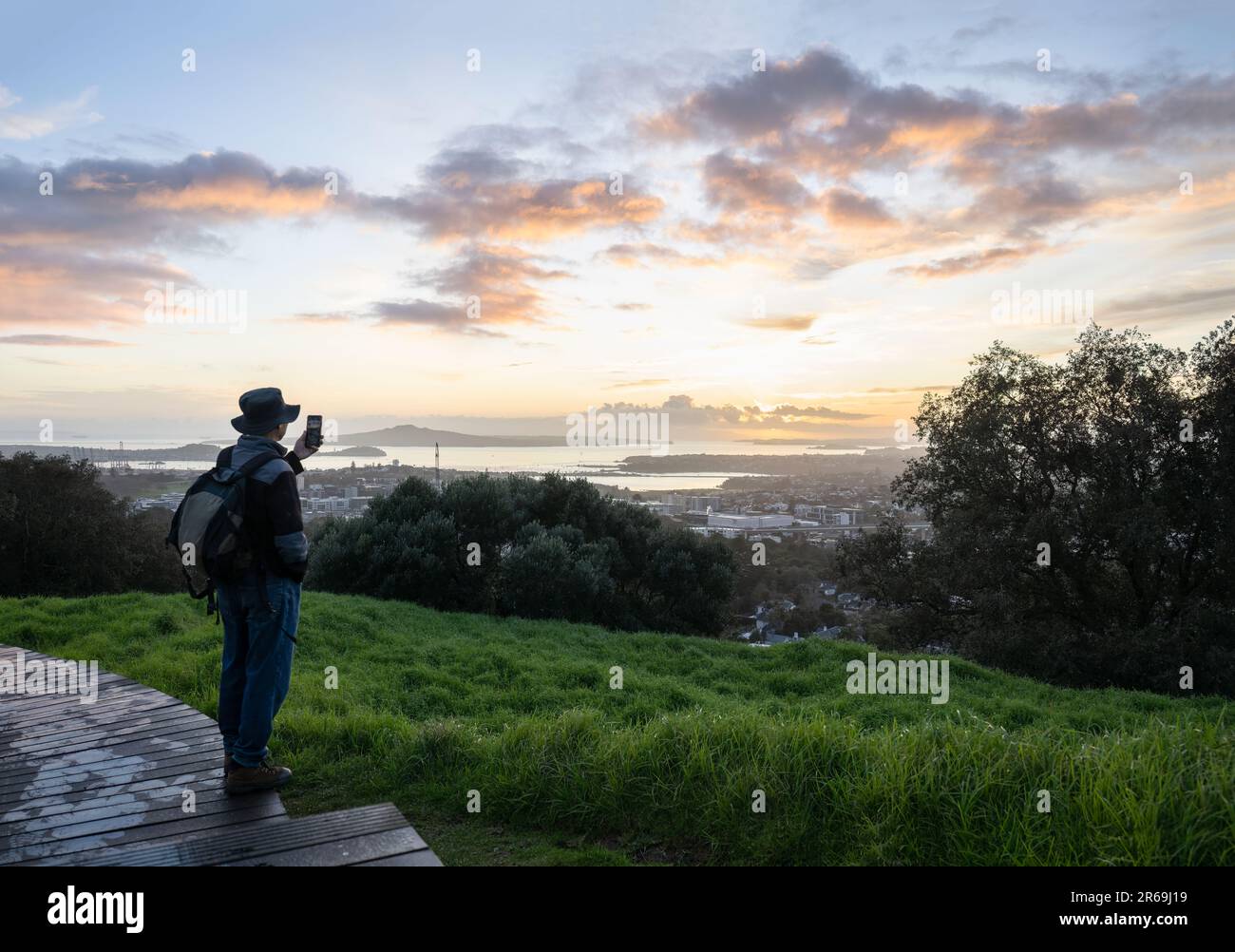 Tourisme prenant des photos avec un smartphone au sommet du Mont Eden au lever du soleil. Rangitoto Island au loin. Auckland. Banque D'Images