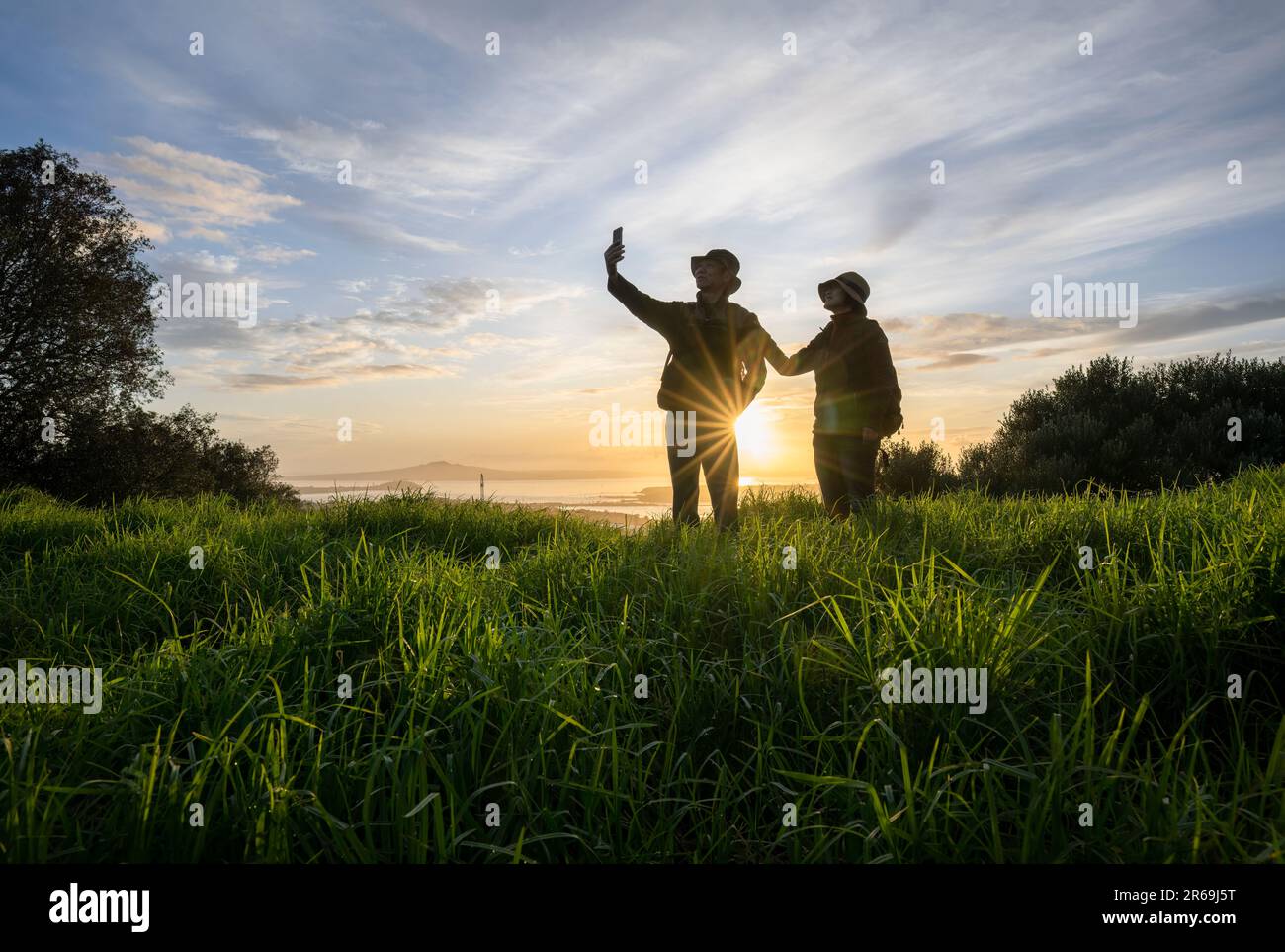 Couple prenant une photo de selfie avec un smartphone au sommet de Mt Eden au lever du soleil. Rangitoto Island au loin. Auckland. Banque D'Images
